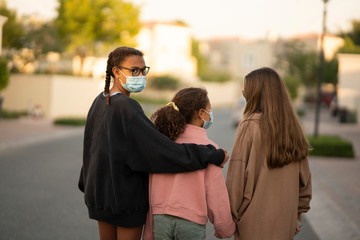 three young teens or preteens walking  on a street wearing street clothes and  surgical face mask to protect against an epidemic of diseases or viruses