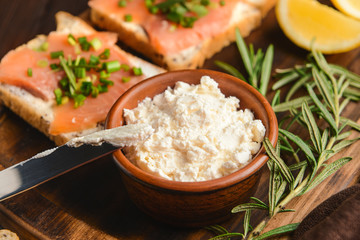Bowl with tasty cream cheese and sandwiches on board, closeup