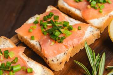 Sandwiches with tasty cream cheese and salmon on board, closeup