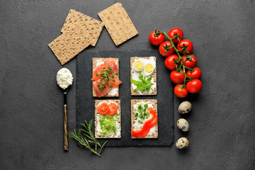 Crispbread with tasty cream cheese, salmon, eggs and vegetables on dark background