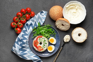 Fresh buns with tasty cream cheese, eggs and vegetables on dark background