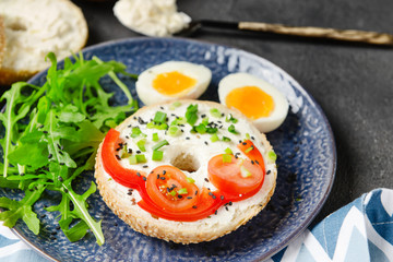 Fresh bun with tasty cream cheese, eggs and vegetables on plate