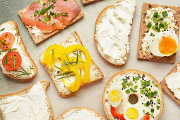 Different sandwiches with tasty cream cheese on light background