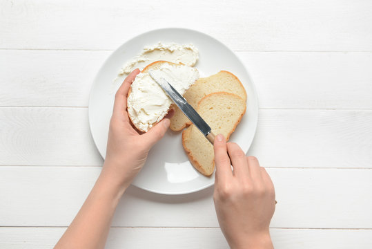Woman making tasty sandwich with cream cheese on white wooden background