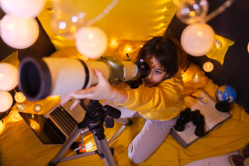 Fototapeta na wymiar Small girl using telescope at home living room in a tent.
