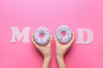 Female hands with tasty doughnuts and word MOOD on color background