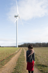 A woman with red skirt walking on the grassland with a windmill in the background