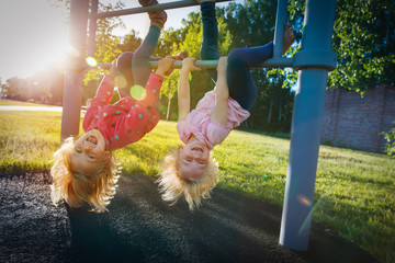 happy cute little girls upside down on monkey bars at sunset