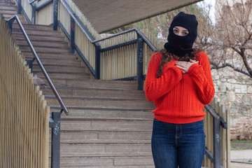 Portrait of attractive caucasian young woman model with ski mask showing shape heart with hands, expressing love, in the park, orange sweater and jeans, long curly hair. Place for your text in copy sp