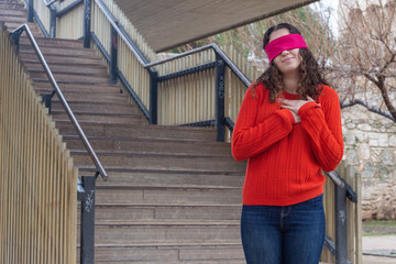 Portrait of attractive caucasian young woman model with eye tape showing shape heart with hands, expressing love, in the park, orange sweater and jeans, long curly hair. Place for your text in copy sp