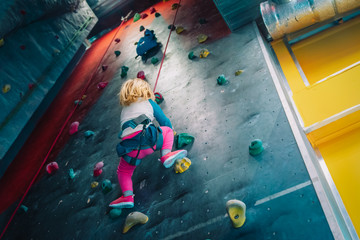 Obraz na płótnie Canvas Little girl climbing on artificial boulders wall in gym
