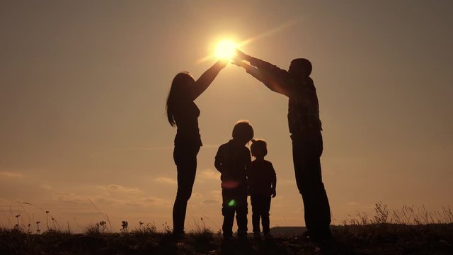 happy family teamwork silhouette shows a house and comfort symbol at sunset. mom dad and kids children portray a house roof hold their hands lifestyle over their heads
