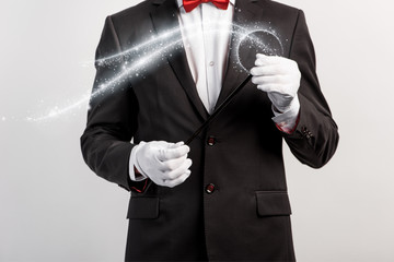 cropped view of magician in suit and hat holding wand isolated on grey with glowing illustration