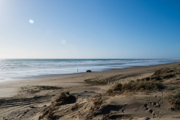 A man outside his truck that he drove on Ninty Mile Beach, North Island, New Zealand. Beautiful,  sandy, very wide, large beach with grass and tire tracks
