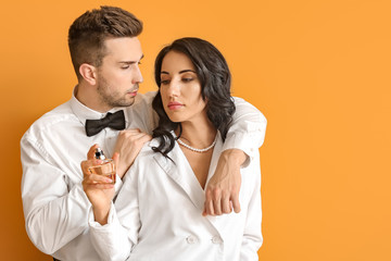Stylish young couple with perfume on color background