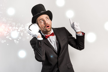 professional magician pointing up and listening to magic ball isolated on grey with glowing...