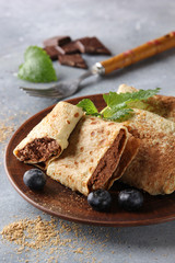 Concept of Russian cuisine. Breakfast. Pancakes with chocolate filling on a brown plate, with fresh berries and mint on a light grey background. Background image, copy space