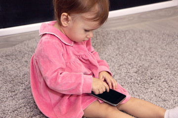 beautiful little girl with a smartphone on the carpet in her room.