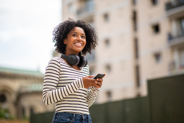 smiling young black woman with mobile phone and headphones outdoor in city