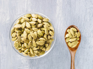 Spice green cardamom (Elettaria cardamomum) in transparent bowl and wooden spoon on gray concrete background closeup. Modern apothecary, naturopathy and ayurveda concept