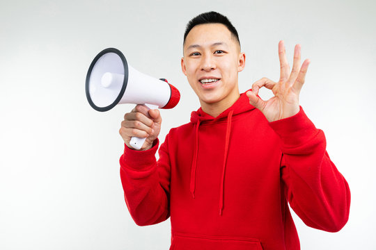 Studio Portrait Of A Young Asian Man In A Red Hoodie With A Loudspeaker In His Hands On A White Background Studio