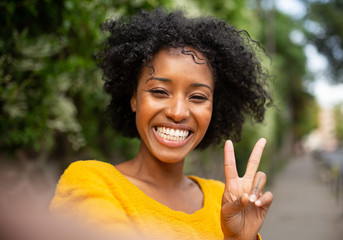 young african woman taking selfie outdoors with peace hand sign