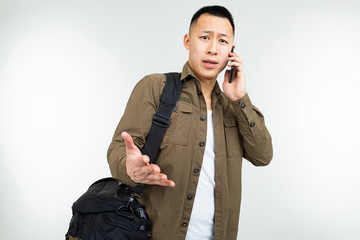 Asian man in urban clothes with a bag communicates using a smartphone about a business on a white background