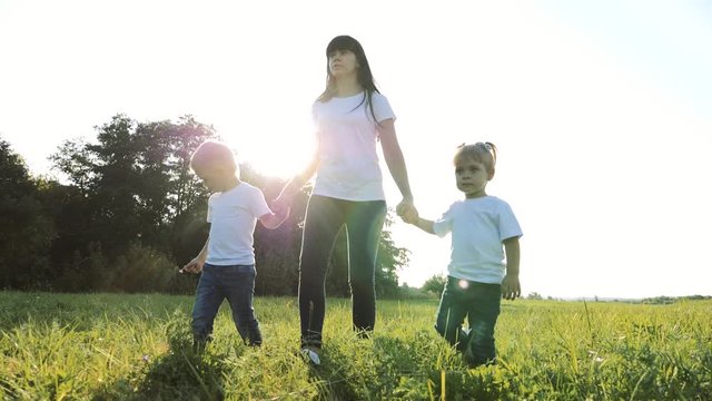 happy family teamwork mother, little brother and sister walk in the park nature holding hands slow motion video concept. mom, kids boy and girl daughter lifestyle and son hold hands go on green grass