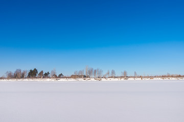 Fototapeta na wymiar A large frozen river covered with even snow. Clear sunny day
