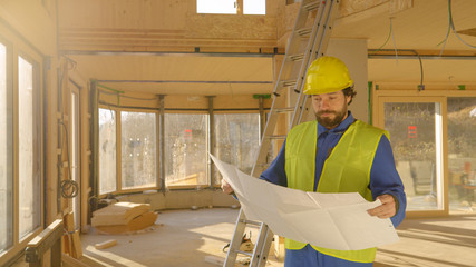 COPY SPACE: Male architect looks at his plans and observes an unfinished house.