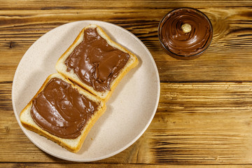 Two slices of bread with delicious chocolate hazelnut spread on wooden table. Top view