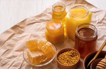 Liquid yellow bee honey in glass jars, pollen and honeycomb on Kraft paper on table