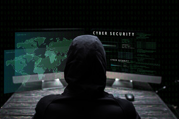 back view of hooded hacker sitting near computer monitors with cyber security lettering on black