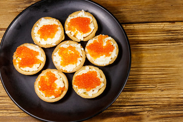 Tartlets with red caviar and soft cheese on a wooden table. Top view