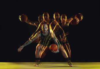 Young basketball player of team in sportwear training, practicing in action, motion isolated on dark background in neon, strobe light. Concept of sport, movement, energy and dynamic, healthy lifestyle