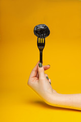black dumpling on a black fork in a female hand on a yellow background
