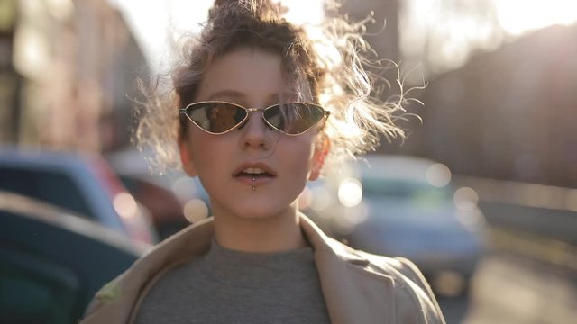 Unconventional woman portrait in sunglasses at the city, wind blowing her hair, slow motion