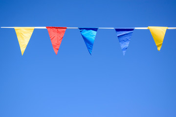 Triangular multi-colored flags hang on a rope. Blue sky background. Concept of a holiday, a party.