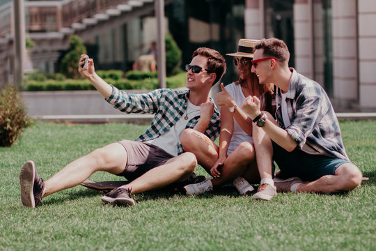 Youth Selfie Sitting On The Grass During A Summer Walk. European Teens Take A Photo With Their Phone On A Sunny Summer Day.