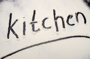 words Kitchen written on a black background with flour. Inscription.