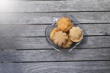 A bowl of Kuih Bahulu or Baulu on wooden table.  Kuih Bahulu or Baulu is also known as Malaysian sponge cake.  Served during festive season such as Hari Raya celebration 