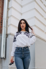 a young girl with brown hair in a white blouse and blue jeans walks down the street