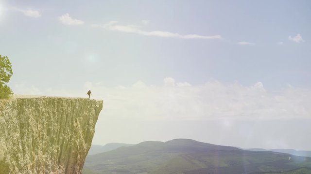 Extreme man comes to the cliff of a high mountain and spreads his arms to the sides in honor of the conquest of the top. A curious tourist stands on the edge of the mountain and admires the scenery.
