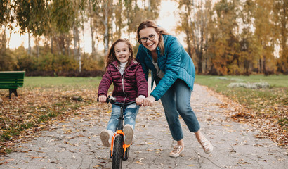 Caucasian mother looking through her eyeglasses is helping her daughter to ride the bike during an...