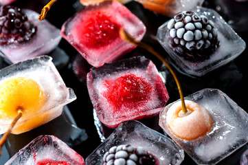  frozen raspberries berries cherries and blackberries in pieces of ice in a glass bowl on a black background