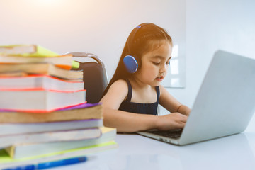 Baby cute girl playing laptops With blurred Large stack of books on foreground. Children and learning concept.