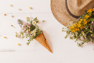 waffle cone with a wild flowers, with straw hat on a white background. Creative design. Top view, flat lay.