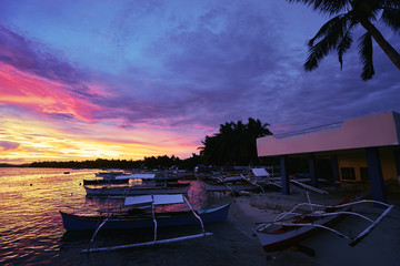 Beautiful colorful sunset on the seashore with fishing boats. Philippines, Siargao Island.