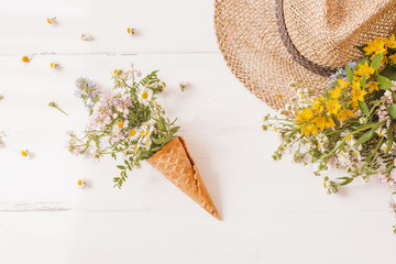 waffle cone with a wild flowers, with straw hat on a white background. Creative design. Top view, flat lay.