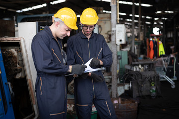 Factory technicians are discussing or planning work. They wear uniforms, safety helmets, and protective goggles. And look at the clipboard with details of the work.